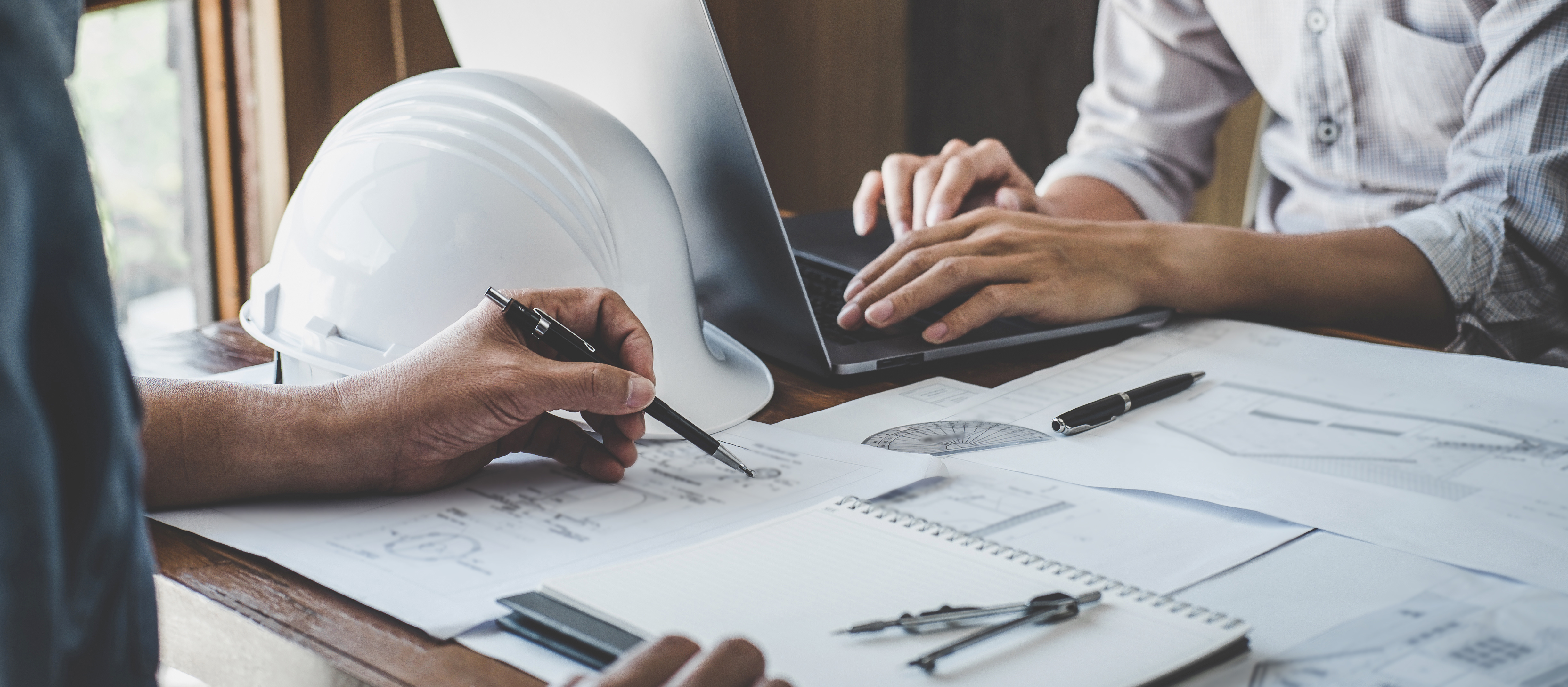 Two people looking over plans with laptop and hardhat