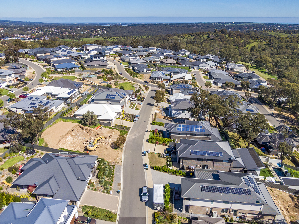 Aerial view of houses and streets in new wealthy suburb in Adelaide foothills with construction in foreground and coastline in background.
